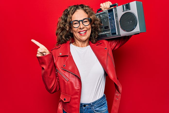 Middle age brunette hipster woman holding retro music boombox ov