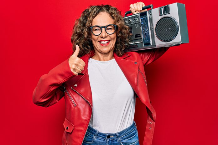 Middle age brunette hipster woman holding retro music boombox ov