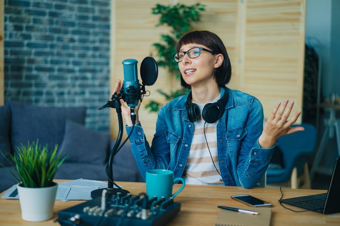Female Blogger Recording Audio In Sound Studio Talking In Microp