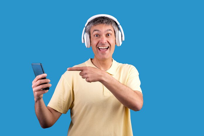 Man With Gray Hair Wearing Headphones Showing Smartphone, Blue B