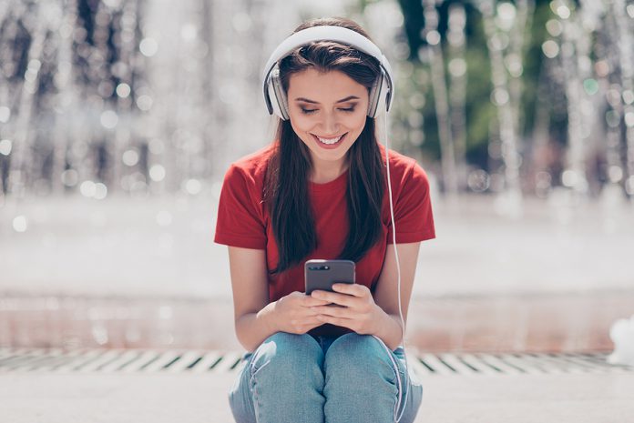 Young And Nice Brunette Girl Sits Near The Fountain In Headphone