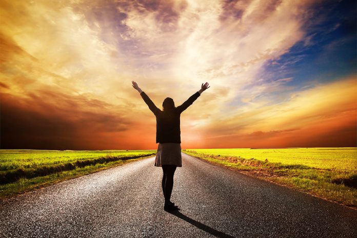 Happy woman standing with hands up on long straight road facing