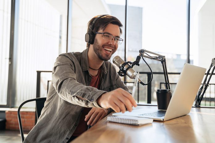 Young Man Host In Headphones And Glasses Enjoying Podcasting In