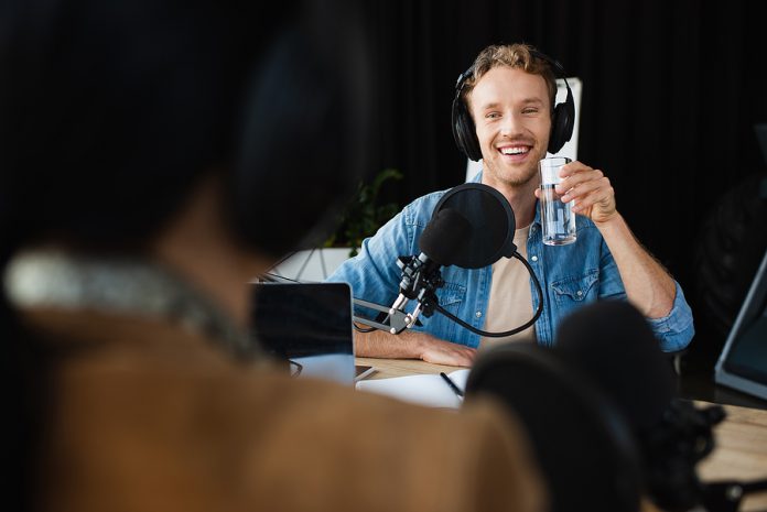 Happy Radio Host In Headphones Looking At Blurred Colleague And