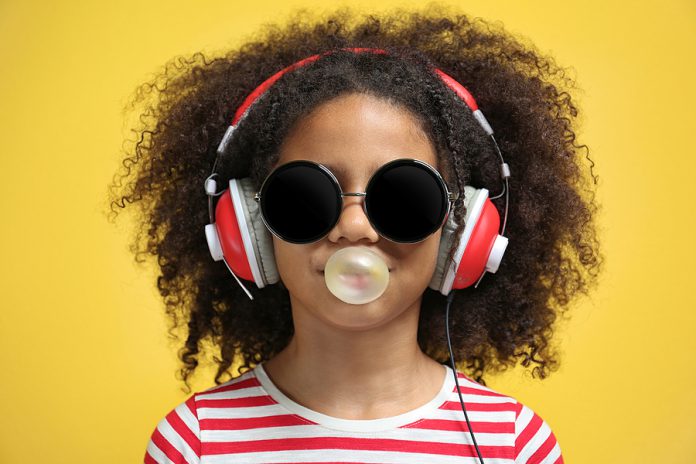Afro-American little girl with headphones and sunglasses chewing